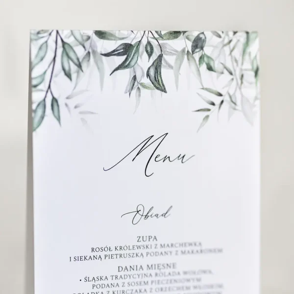 Stojące menu weselne z dekoracyjnym wzorem zielonych liści, prezentowane na stole.