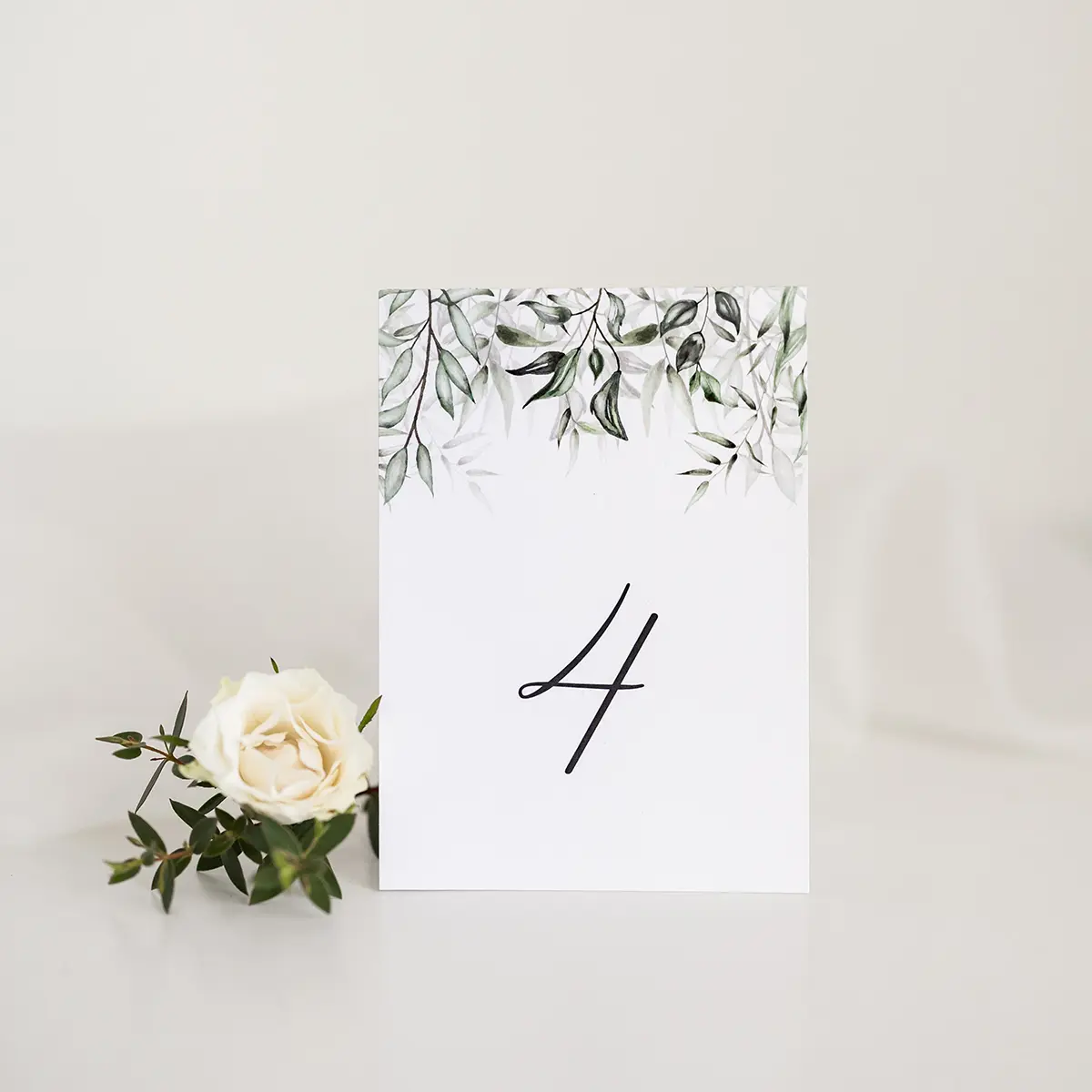 Stylowy numer stołu z zielonymi liśćmi, idealnie pasujący do naturalnej i eleganckiej aranżacji wesela.