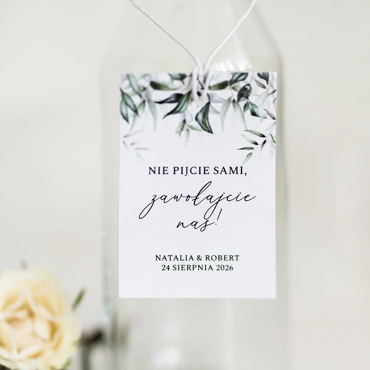 Detal zawieszki na butelkę z eleganckim zielonym wzorem, przywiązanej delikatnym sznurkiem do szklanej butelki z korkiem.