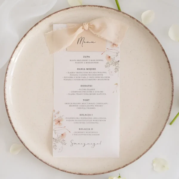 Subtelne menu ślubne na kalce z motywem kwiatowym, wyeksponowane na ceramicznym talerzu.