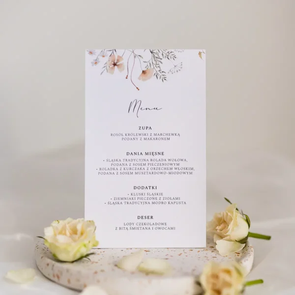 Stojące menu weselne z delikatnym kwiatowym wzorem i elegancką czcionką, ozdobione kremowymi różami.