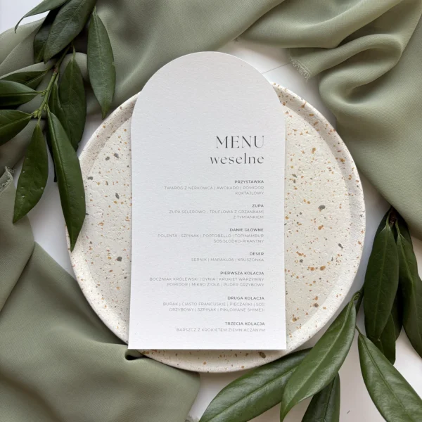 Menu ślubne Jungle w kolorze złamanej bieli, prezentowane na dekoracyjnym talerzu z liśćmi i tkaniną w tle.