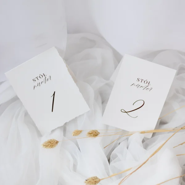 Dwa warianty numerów stołów z kolekcji Róża: jeden na gładkim białym papierze, drugi z postrzępionym brzegiem. Elegancki minimalizm i delikatna typografia.