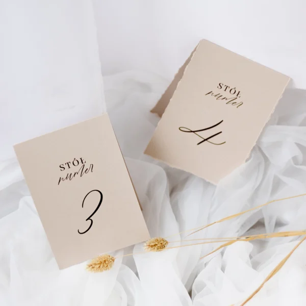 Stylowe numery stołów na gładkim papierze w odcieniu ciasteczkowym. Klasyczna forma i elegancka czcionka doskonale wpisują się w romantyczną estetykę.