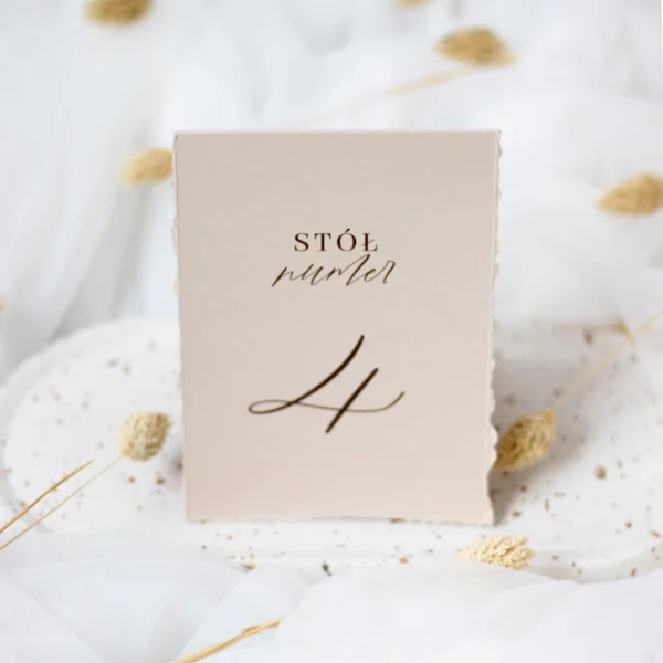 Numery stołów w kolorze ciasteczkowego beżu, ozdobione subtelnym liternictwem i delikatnie postrzępionym brzegiem papieru.