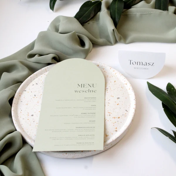 Zestaw menu weselnego i winietki Jungle w zielonej tonacji, ułożony na talerzu z liśćmi w tle.