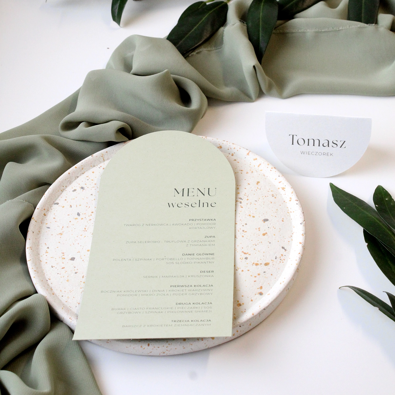 Zestaw menu weselnego i winietki Jungle w zielonej tonacji, ułożony na talerzu z liśćmi w tle.