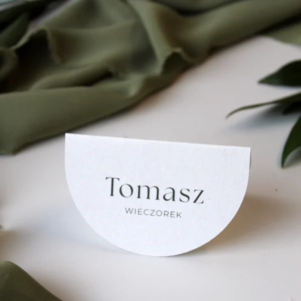 Winietka weselna Jungle w kolorze złamanej bieli, prezentowana na tle zielonych tkanin i liści.