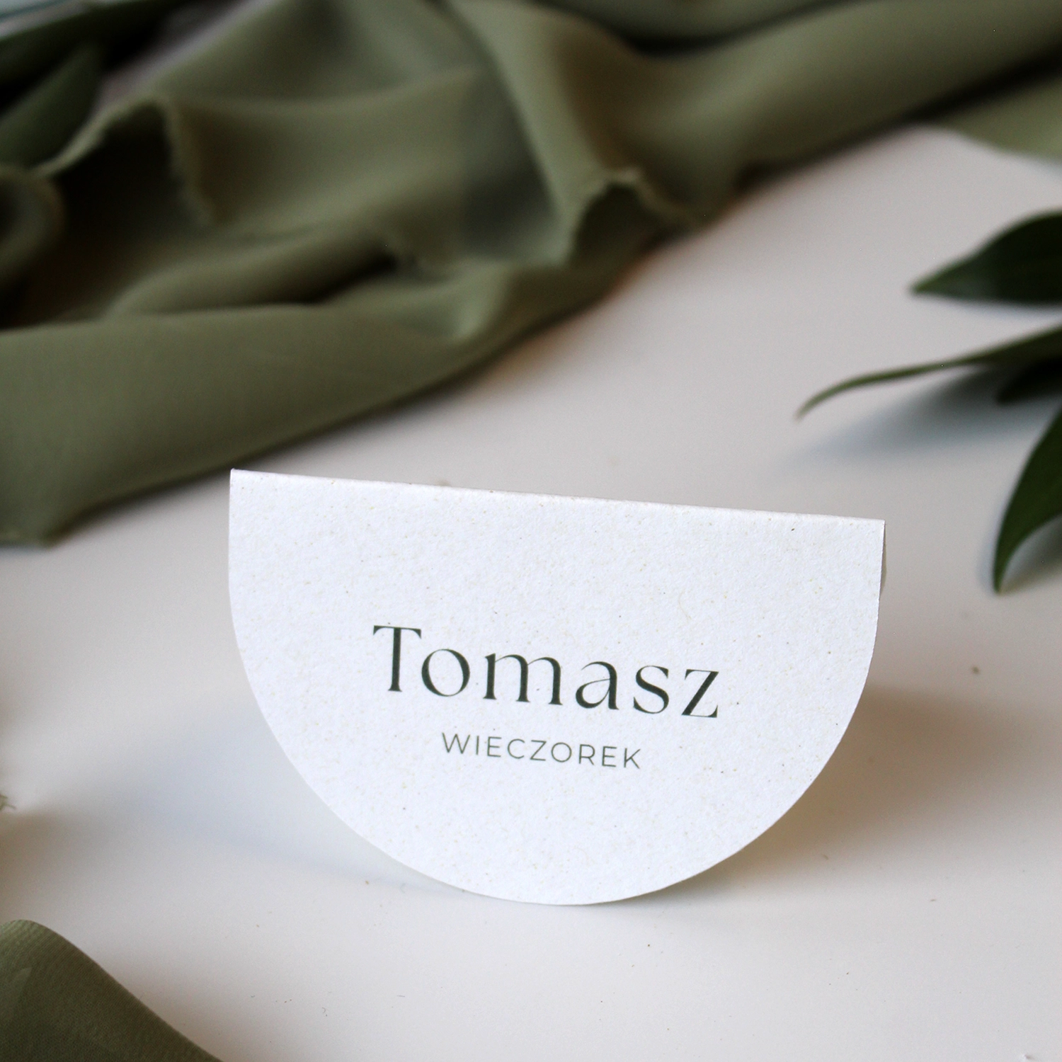 Winietka weselna Jungle w kolorze złamanej bieli, prezentowana na tle zielonych tkanin i liści.