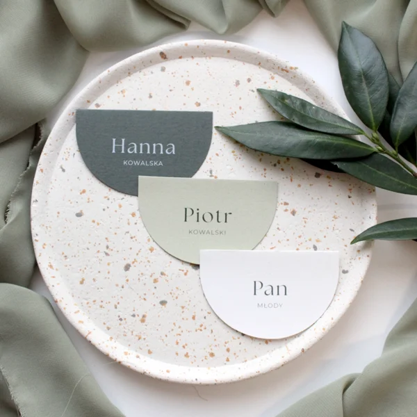 Półokrągłe winietki ślubne z kolekcji Jungle w odcieniach zieleni i złamanej bieli, ułożone na dekoracyjnym talerzu.