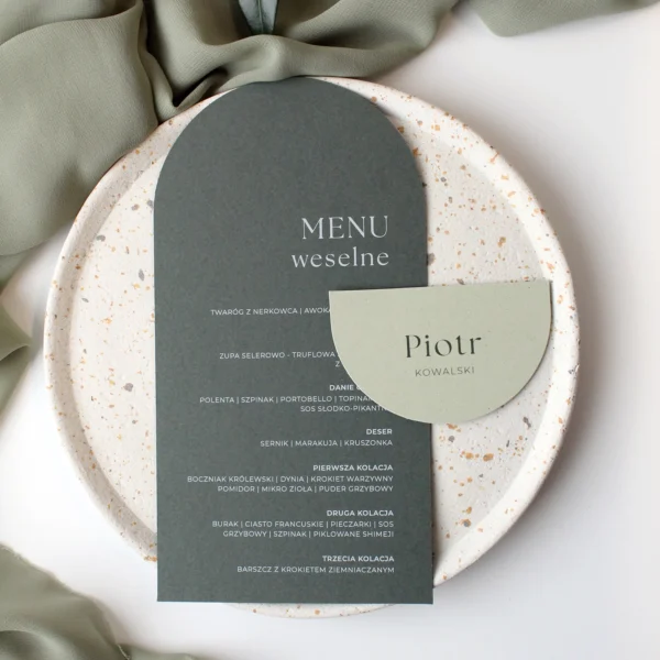 Komplet winietki i menu ślubnego Jungle w zielonych odcieniach, ułożony na talerzu w naturalnej aranżacji.