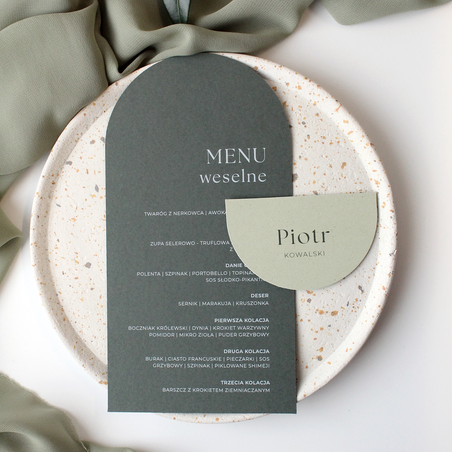 Komplet winietki i menu ślubnego Jungle w zielonych odcieniach, ułożony na talerzu w naturalnej aranżacji.