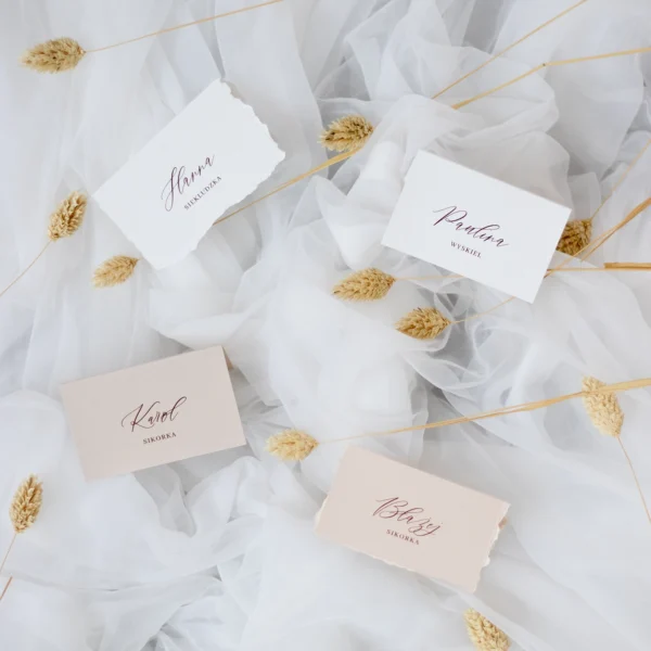 Dwie prostokątne winietki z beżową wstążką, jedna biała, druga w odcieniu nude, zaprezentowane na owalnym talerzu.