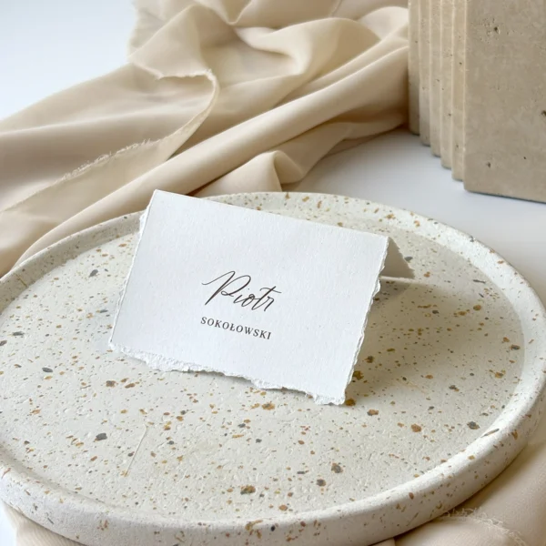 Winietka w formie daszka z białego ekologicznego papieru o postrzępionych brzegach, ustawiona na owalnym talerzu.