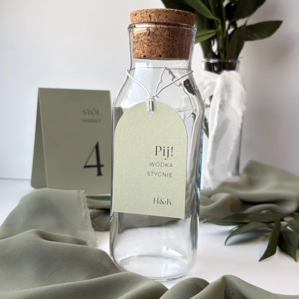 Zawieszka na butelkę z kolekcji Jungle w odcieniu jasnej zieleni, z napisem „Pij! Wódka stygnie” i inicjałami pary młodej.