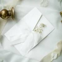 Zaproszenie w folderze ozdobione szarpaną wstążką i suszoną gipsówką