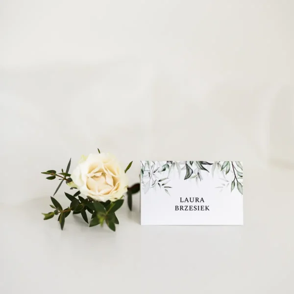 Winietki na wesele w stylu botanicznym, z zielonym motywem liści, ułożone na jasnym tle z kwiatowymi dodatkami.