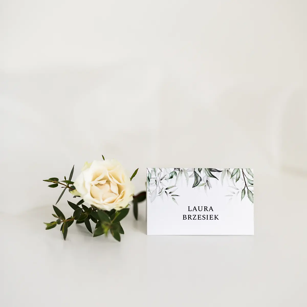 Winietki na wesele w stylu botanicznym, z zielonym motywem liści, ułożone na jasnym tle z kwiatowymi dodatkami.