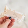 Elegancka winietka na stół wykonana z kalki z subtelnym kwiatowym motywem i delikatnym beżowym paskiem na imię i nazwisko gościa.