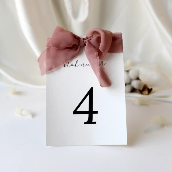 Numer stołu ozdobiony szarpaną wstążką w odcieniu różu, idealny jako elegancki dodatek na stół weselny.