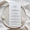 Minimalistyczne menu weselne w odcieniach ecru, prezentowane na jasnym tle z delikatnymi dodatkami dekoracyjnymi.