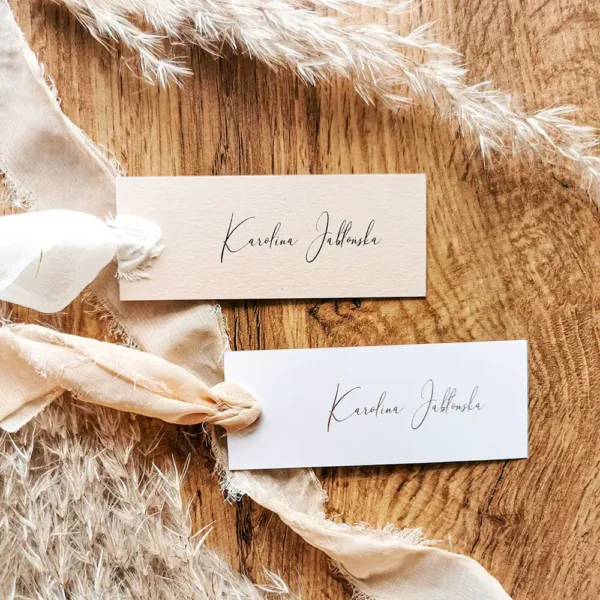 Komplet beżowej i białej winietki z imionami, ozdobionych postrzępionymi szyfonowymi wstążkami.