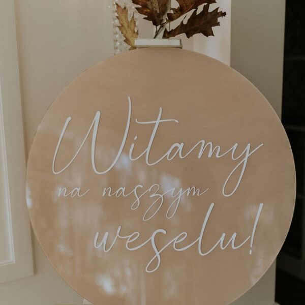 Okrągła tablica powitalna w kolorze beżowym.