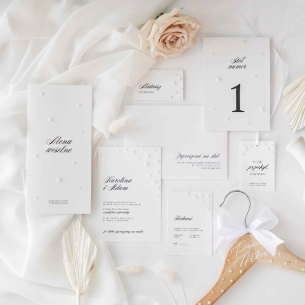 Zaproszenia ślubne o perłowym motywie ukazane na delikatnym białym materiale wraz z delikatnymi ozdobami