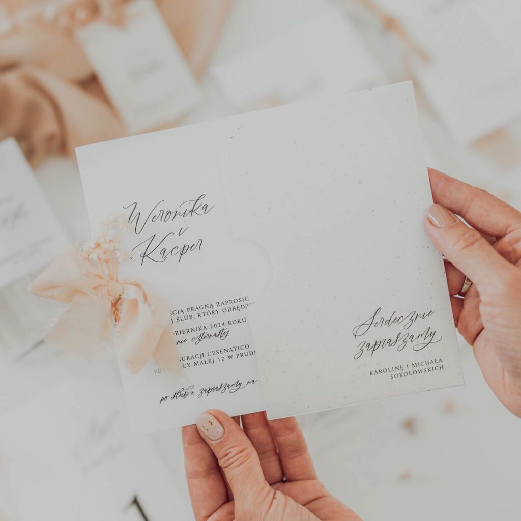 Zaproszenia ślubne, biel ze zdobieniami i kwiatami oraz wstążką