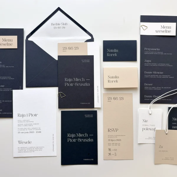 Zaproszenia ślubne z kolekcji Navy Blue w granatowo-beżowej kolorystyce z elegancką typografią i dodatkami, ułożone na jasnym tle.