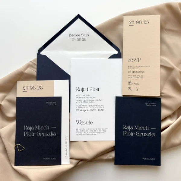 Zestaw zaproszeń ślubnych Navy Blue z kopertą i kartami RSVP, ułożony na tkaninie w kolorze piaskowym.