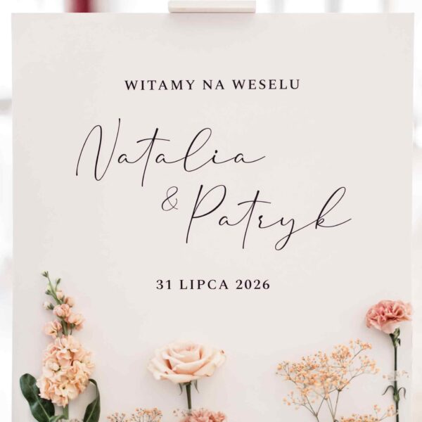 Kwiatowa tablica powitalna ustawiona na białej drewnianej sztaludze na tle sali weselnej