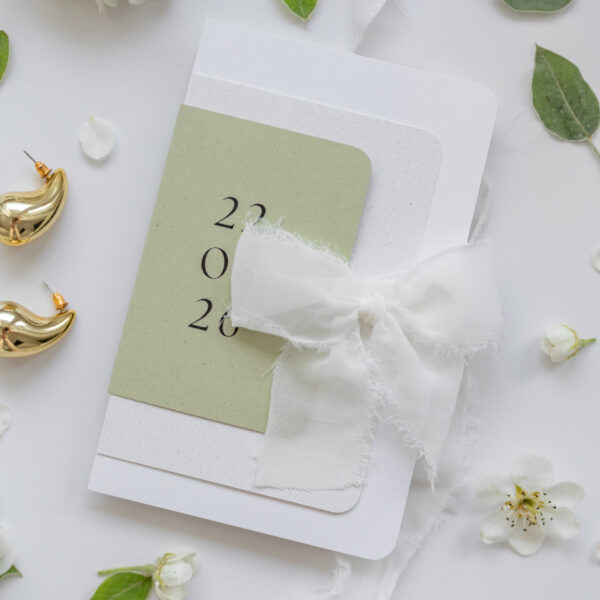 Zaproszenie weselne w kolorze oliwkowej zieleni i bieli z materiałową wstążką - Willa Słoneczna, na tle świeżych kwiatów i złotej biżuterii