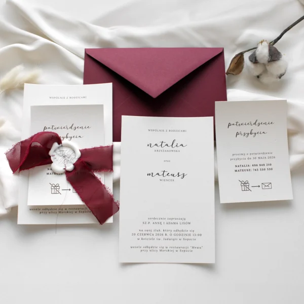 Eleganckie zaproszenia ślubne z bordową szarpaną wstążką i białą pieczęcią lakową, w towarzystwie koperty w kolorze burgundu.