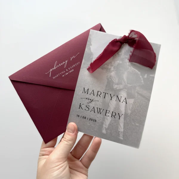 Zaproszenie ślubne ze zdjęciem pary młodej na kalkowym papierze, ozdobione burgundową wstążką i dopasowaną kopertą.