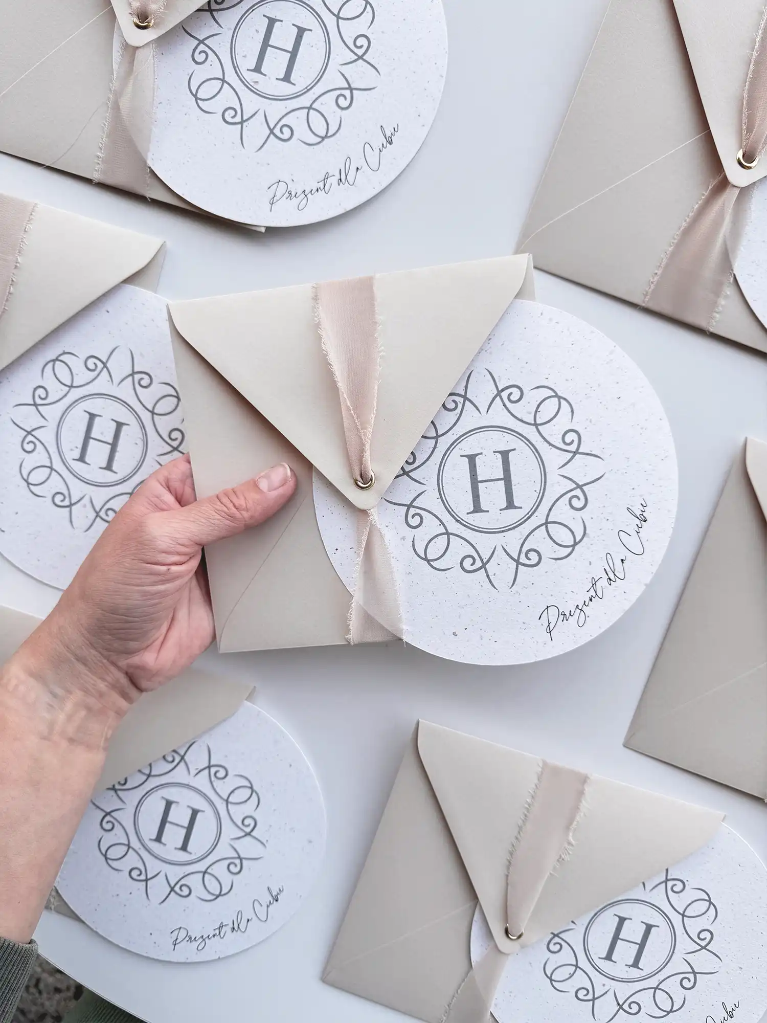 Elegancki, okrągły voucher podarunkowy z personalizowanym nadrukiem w delikatnej, beżowej kopercie z wstążką.