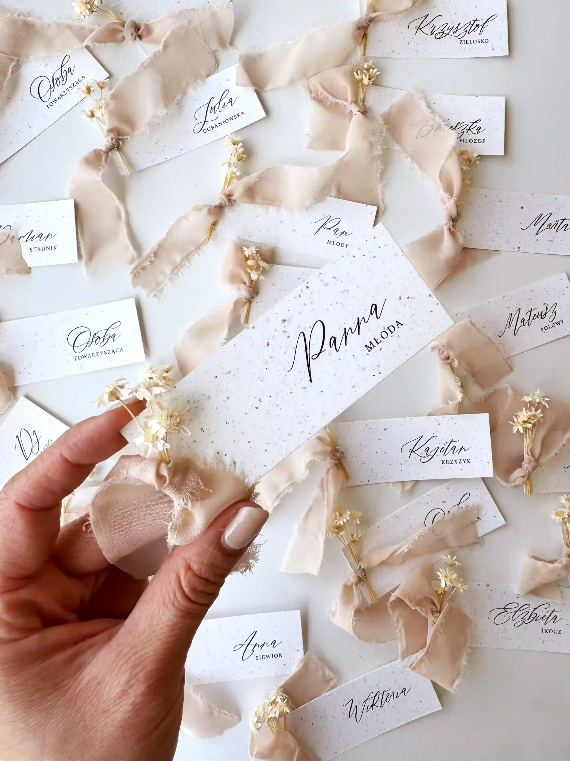 Personalizowane płaskie winietki ślubne w jasnej kolorystyce przewiązane jasnym materiałem