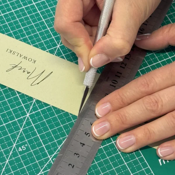 Zielona mata samoregenerująca z metalową linijką i nożykiem introligatorskim, przygotowana do cięcia papierowych winietek ślubnych.