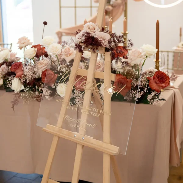 Elegancka tablica powitalna z kolekcji Złoty Folder, wykonana z przezroczystego plexi ze złotym napisem.