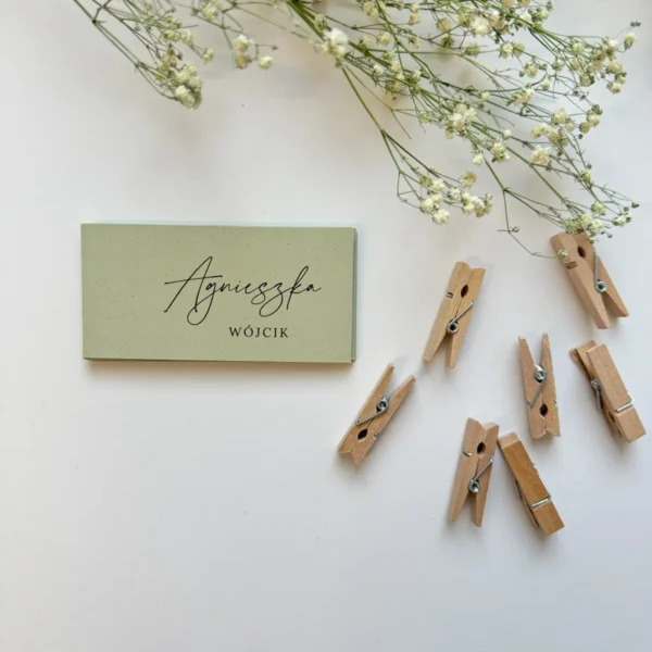 Eleganckie zielone winietki ślubne na białym tle, udekorowane suszoną gipsówką i przymocowane drewnianą klamerką.