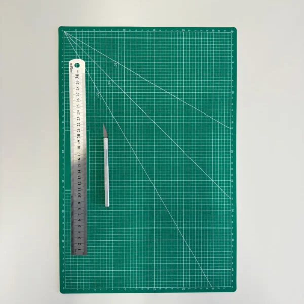 Zielona mata do cięcia papieru z metalową linijką i nożykiem introligatorskim, idealna do precyzyjnego przygotowania winietek ślubnych DIY.