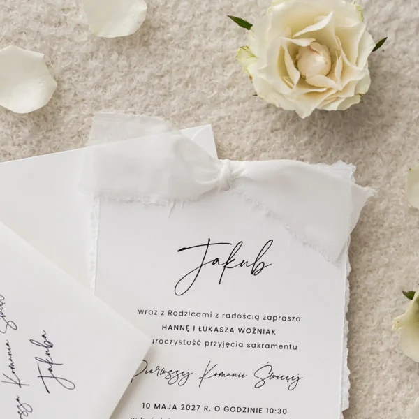 Białe zaproszenie komunijne z szarpanymi brzegami, ozdobione kokardą z szyfonowej wstążki, w eleganckim stylu.