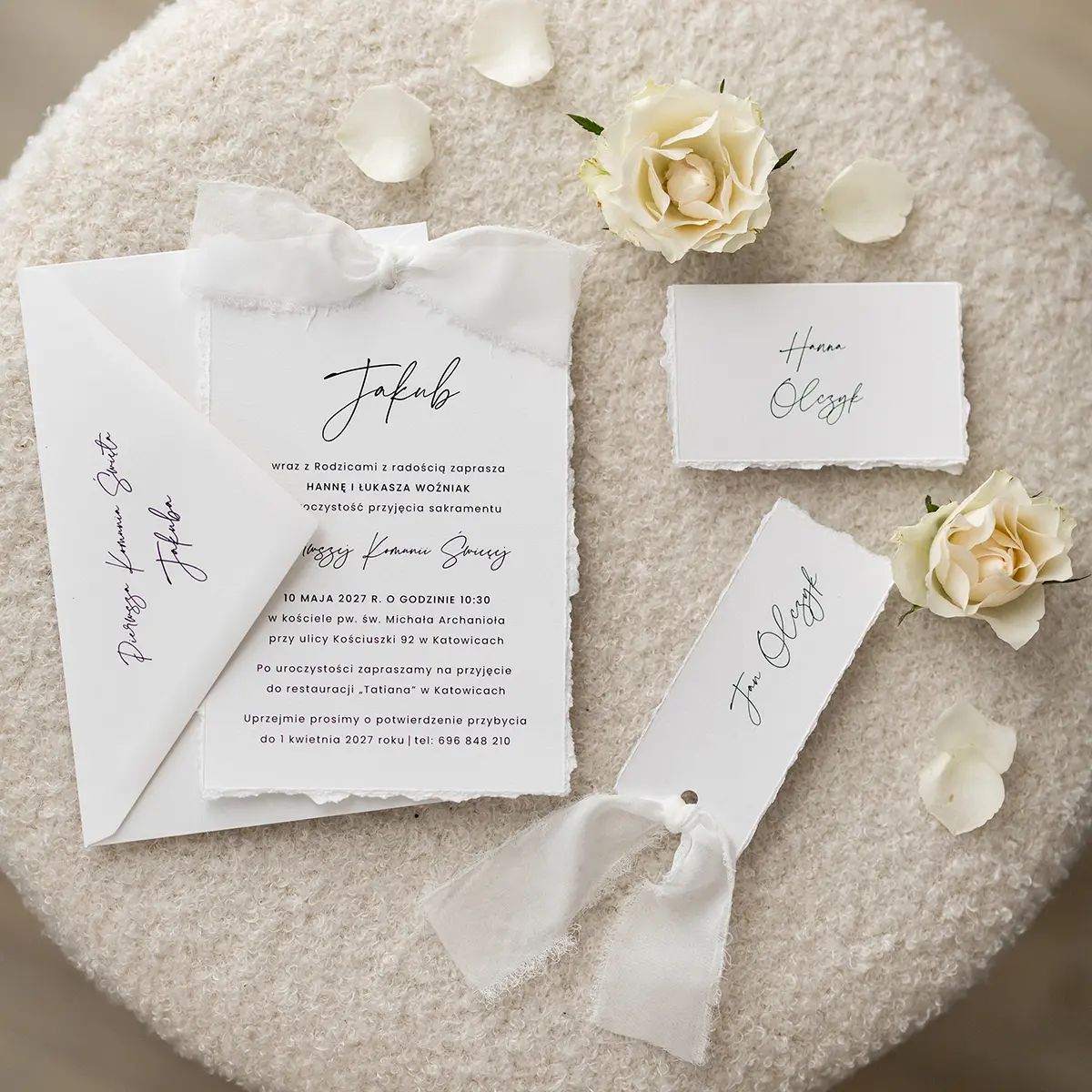 Komplet białych zaproszeń na Pierwszą Komunię Świętą z ozdobnymi wstążkami i dopasowanymi winietkami.
