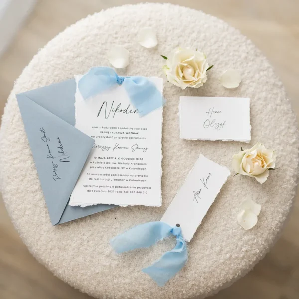 Zestaw niebieskich zaproszeń komunijnych z szyfonowymi wstążkami, dopasowanymi kopertami i stylowymi detalami.