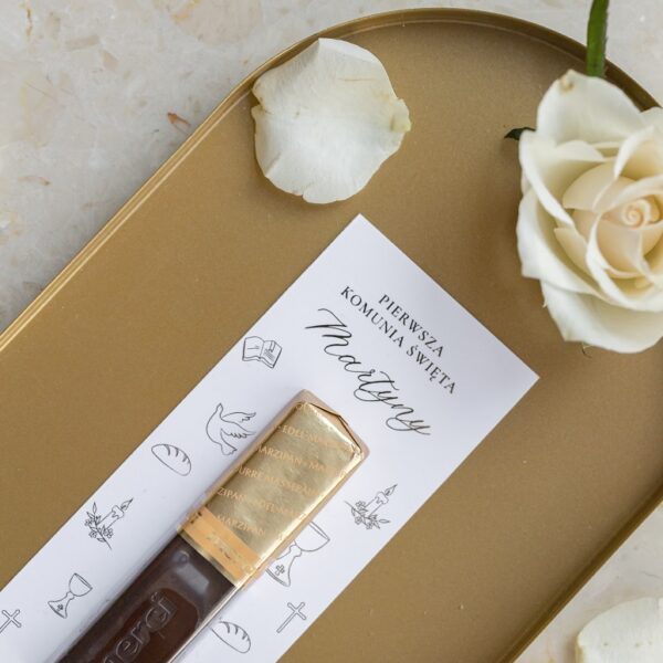 Upominek na komunię – czekoladka Merci przymocowana do białej karty z napisem Pierwsza Komunia Święta Martyny i dekoracją z białych róż.