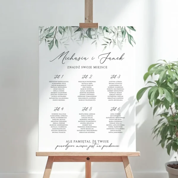 Plan stołów na wesele z motywem zielonych liści, ustawiony na sztaludze, elegancki design z czarnym napisem na białym tle.