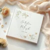 Elegancka księga gości weselnych z personalizowaną okładką, ozdobiona delikatnym kwiatowym motywem.