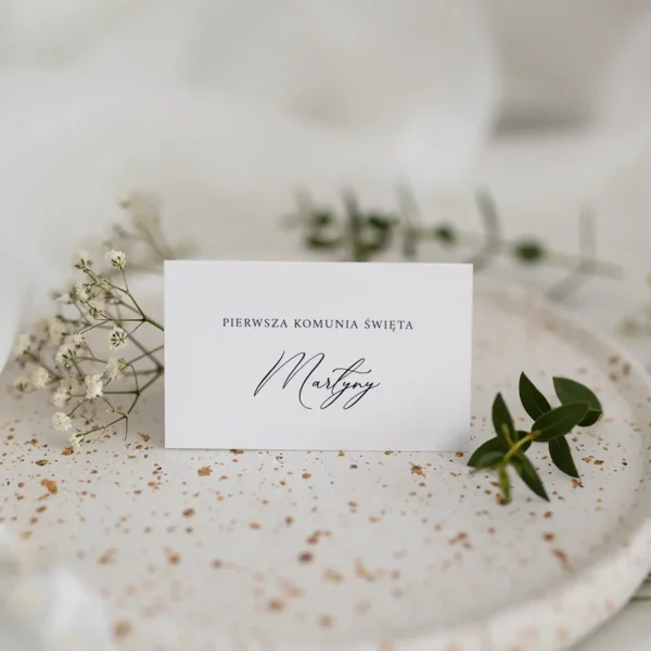 Tył białej winietki komunijnej na tle białego materiału i gipsówki.