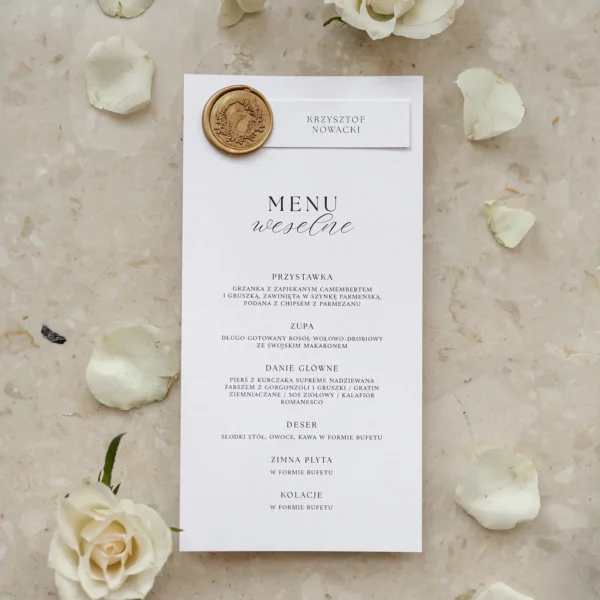 Leżące menu weselne z opaską imienną i złotą pieczęcią, w otoczeniu płatków kwiatów