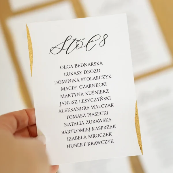 karta z listą gości przy stole 8 trzymana w dłoni, z widocznym złoconym brzegiem